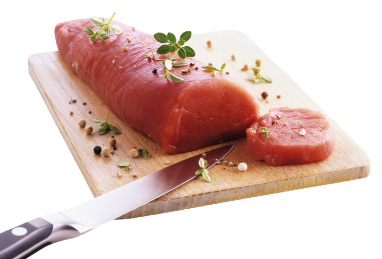 Zu sehen ist ein großes Stück Schweinefilet auf einem Holzschneidebrett mit Messer. Das Fleischstück ist rosa, knochenlos und weitgehend fettfrei. Vor dem Fleisch liegt ein bereits abgeschnittenes schmaleres Stücke des Filets. Dekoriert ist das Filet mit grobem schwarzem Pfeffer und Kräutern.